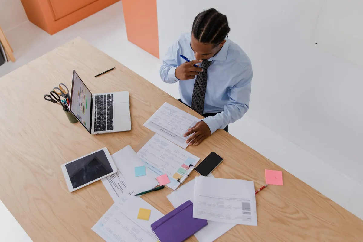 Overhead view of an office desk covered in printed reports beside a laptop and tablet