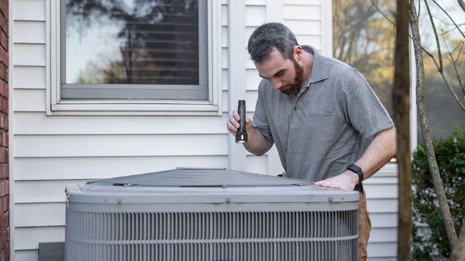Technician inspecting an outdoor air conditioning unit beside a house
