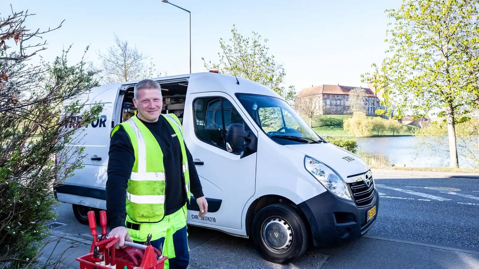 Smiling home service worker carrying a red toolbox beside a white work van