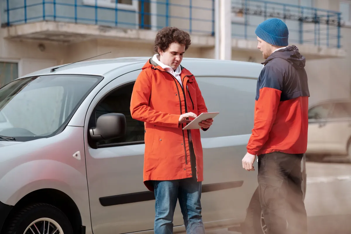 Service worker reviewing a job on a tablet with a customer beside a van