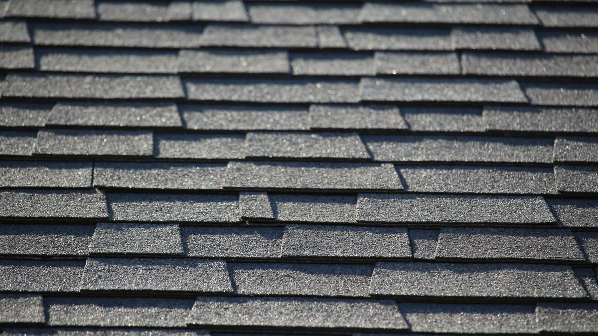 Close-up of rows of gray asphalt shingles on a sloped roof in bright sunlight